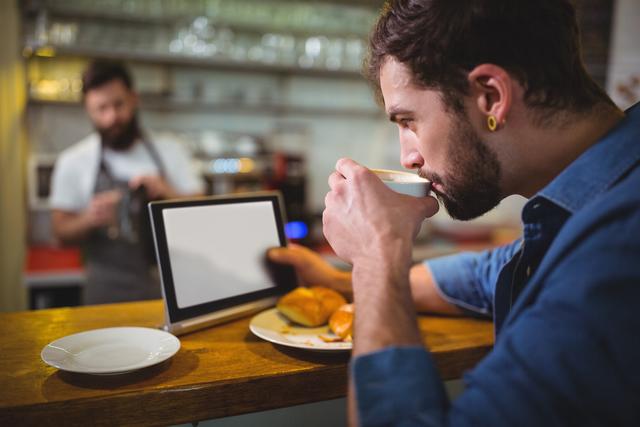 Man sitting at counter and using digital tablet while having coffee in cafÃ©