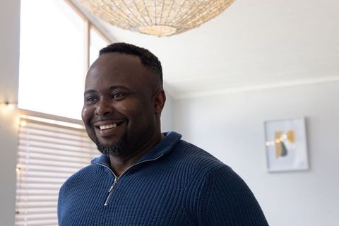Smiling african american man standing in bright modern living room wearing blue sweater