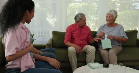 Elderly couple celebrating with family, unboxing gift on couch