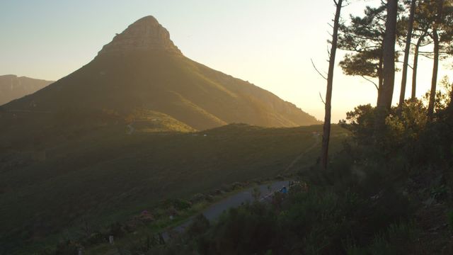 Peaceful sunrise casting golden light over rural mountain road, ideal for travel and nature themes. Suitable for tourism brochures, adventure magazines, and environmental awareness campaigns, emphasizing beauty and tranquility in natural landscapes.