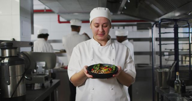 Portrait of caucasian female chef presenting dish and looking at camera. Working in a busy restaurant kitchen.