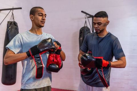 Young boxers adjusting gloves and hand wraps in gritty boxing gym with hanging bags