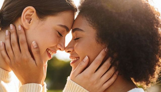 Sunlit intimate moment between two women touching foreheads and smiling in park at golden hour