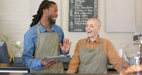 Diverse baristas collaborating over tablet behind counter with croissant display