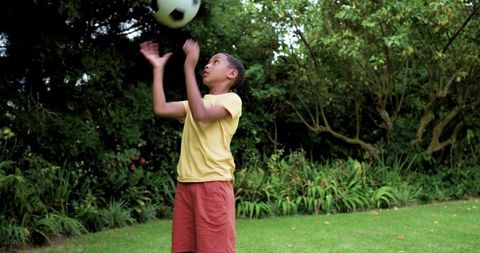 African american boy tossing soccer ball in lush backyard garden