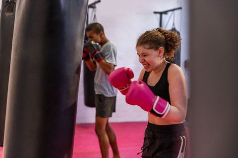 Teen girl boxing and training on heavy bag with male partner in vibrant gym
