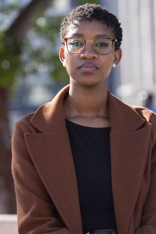 Confident african professional standing in urban area wearing glasses brown coat