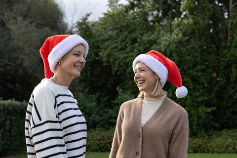Two women chatting outdoors wearing santa hats on garden lawn, holiday cheer