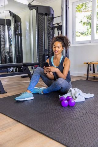 African American Woman Exercising with Smartphone in Home Gym