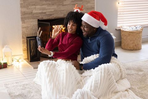African american couple snuggling by fireplace under chunky blanket during holiday video call