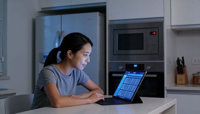 Focused asian woman working on tablet at modern kitchen island, evening glow, stainless appliances