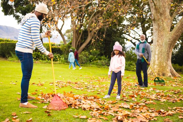 Multi-generation family enjoying time together raking autumn leaves in a park. Ideal for themes of family bonding, outdoor activities, seasonal changes, and nature. Perfect for use in advertisements, family-oriented content, and lifestyle blogs.