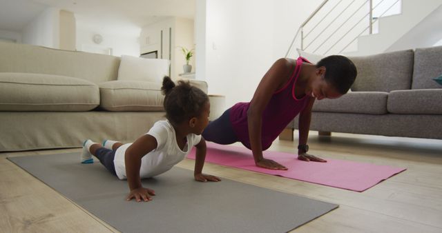 Mother and daughter practicing exercise in living room on yoga mats. Purple and gray mats placed on hardwood floor. Teaches importance of fitness and healthy lifestyle. Ideal for promoting family bonding, health and wellness products, home workout routines.