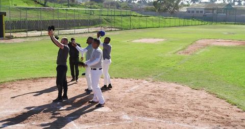 Diverse baseball teammates raising caps at home plate on sunny field celebrating together