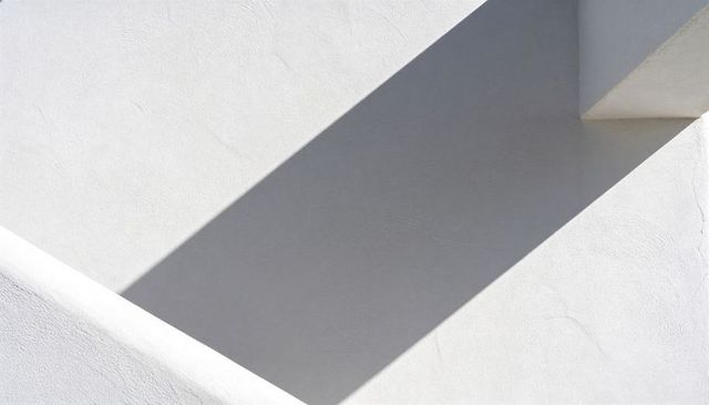 Minimalist white stucco facade casting diagonal shadow on geometric architectural planes