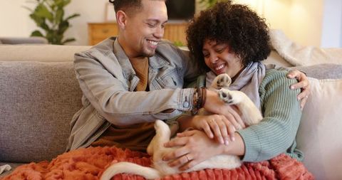 Smiling diverse couple cuddling puppy on couch in cozy living room