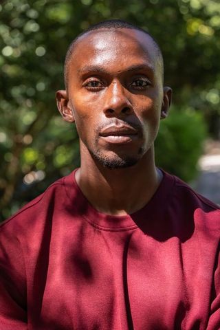 African american man wearing maroon sweatshirt looking at camera in sunlit park portrait