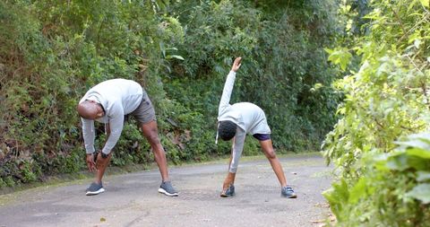 African american father and son stretching together on woodland trail in hoodies