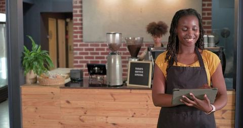 African american barista smiling and using tablet behind rustic brick café counter