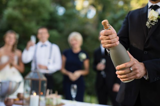 Mid section of groom opening champagne bottle at park