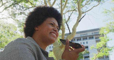 Happy businesswoman having phone conversation outdoors among green trees