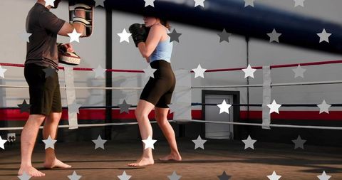 Female boxer practicing punches with coach holding focus mitts in boxing ring