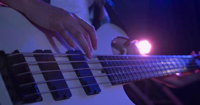 Close-up of a musician's hand playing an electric bass guitar on stage with dramatic lighting, perfect for illustrating concert promotions, music blogs, entertainment posters, and live performance ads.