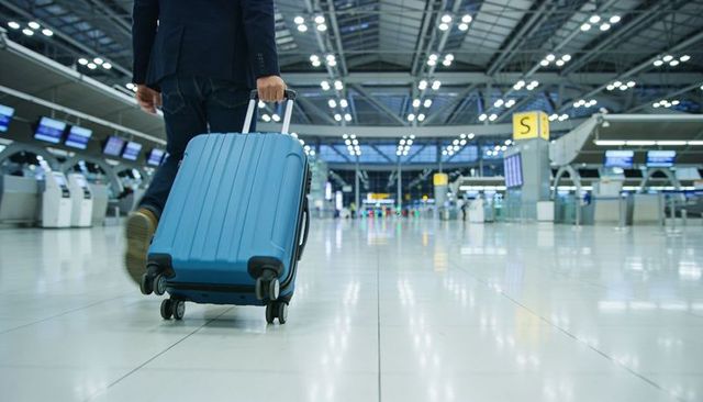 Business traveler walking through modern airport terminal pulling blue carry-on luggage