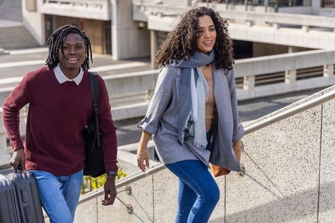 Young diverse friends climbing urban ramps with luggage, smiling travelers heading to terminal