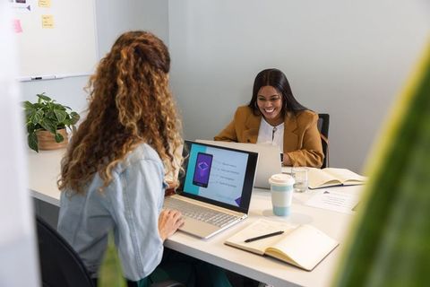 Diverse female coworkers collaborating on app mockup at modern office meeting table