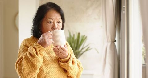 Senior woman enjoying tea by the window in cozy sweater