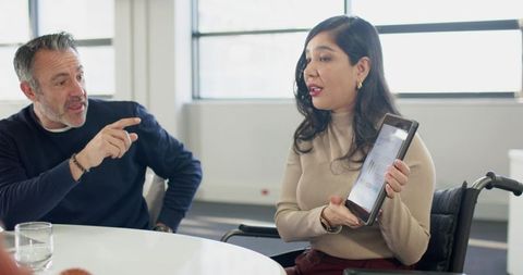 Businesswoman in wheelchair presenting tablet to coworker during collaborative meeting