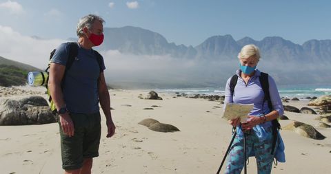 Senior Couple Hiking on Beach with Masks and Maps