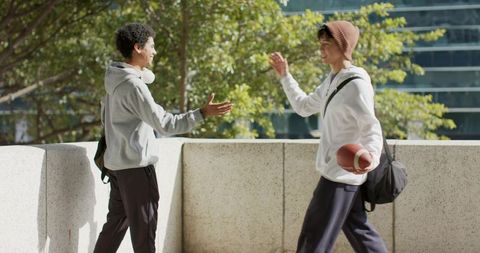 Multicultural teen friends greeting on urban terrace carrying football and backpack