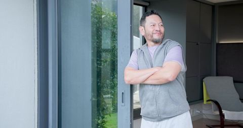Relaxed asian man enjoying garden view through home glass doors