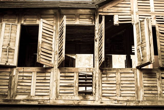 An image showcasing an abandoned wooden old house with open windows. The dilapidated structure exudes an eerie, historic charm, appealing for use in themes involving history, rustic aesthetics, decay, desolation, and vintage architecture. Suitable for storytelling purposes, artistic projects, backgrounds, and documentaries on urban exploration or historic preservation.