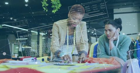 Designers collaborating with augmented reality overlays on fabric table in fashion studio