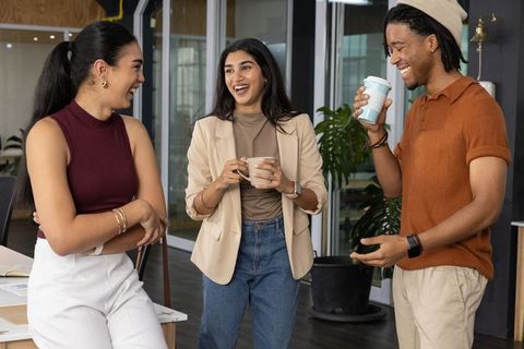 Young professionals laughing and chatting during coffee break in modern coworking office