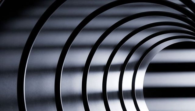 Concentric reflective metal rings forming spiral tunnel, casting dramatic shadow bands
