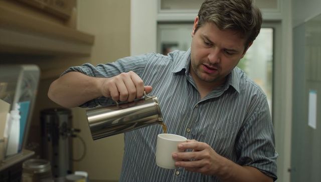 Man pouring coffee from stainless steel carafe into white mug home kitchen morning routine
