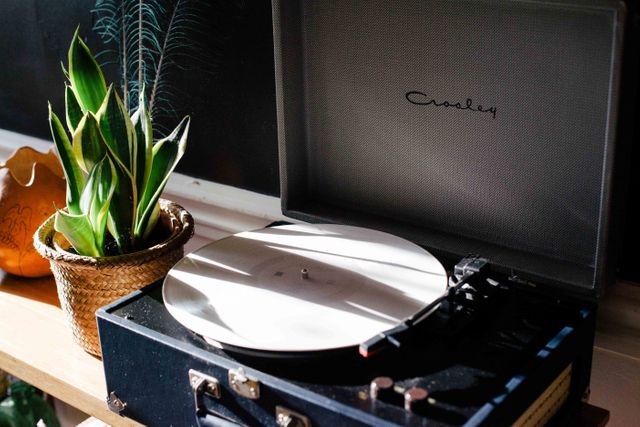 Vintage record player turning in cozy interior setting with indoor plant on wooden shelf. Ideal for concepts related to home decor, vintage lifestyle, nostalgic music, and cozy living spaces.