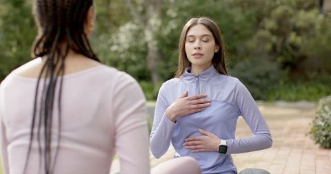 Two women practicing guided breathing outdoors on patio with yoga mat and smartwatch
