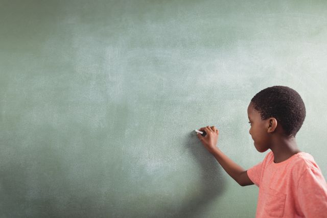 Schoolboy writing on chalkboard in classroom