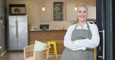 Smiling bald woman cafe owner standing at door welcoming customers in rustic coffeehouse