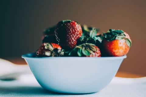 Fresh ripe strawberries overflowing in pale blue bowl with moody bokeh and soft light