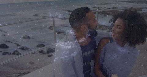 Romantic couple enjoying seaside evening wrapped in blanket