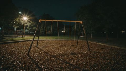 Deserted swing set in quiet night park illuminated by streetlamp