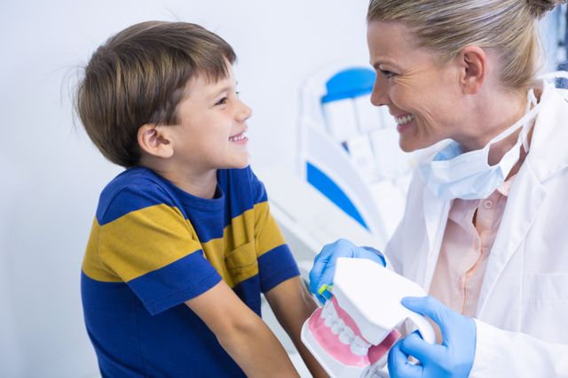 Happy dentist holding dental mold while looking at boy in clinic