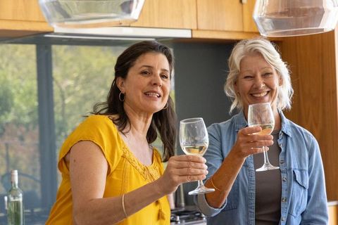 Diverse mature women toasting white wine in cozy modern kitchen celebrating friendship