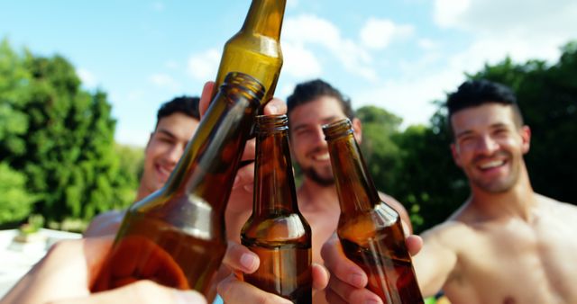 Young men clinking beer bottles while enjoying a sunny day outdoors. Perfect for themes related to friendship, celebration, relaxation, summer events, outdoor gatherings, and socializing.